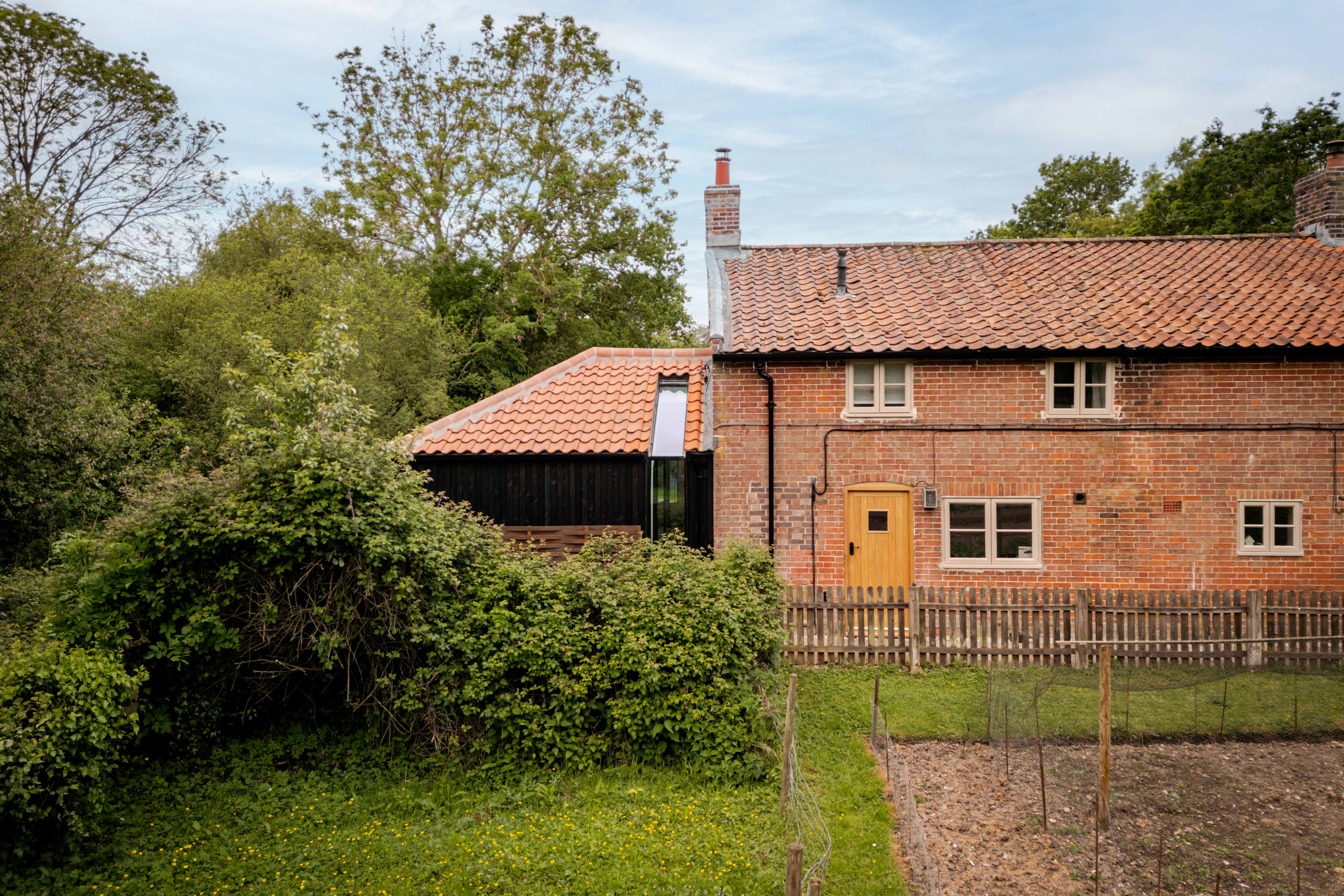 Cambrills, a restored brick cottage and its garden among trees in Suffolk