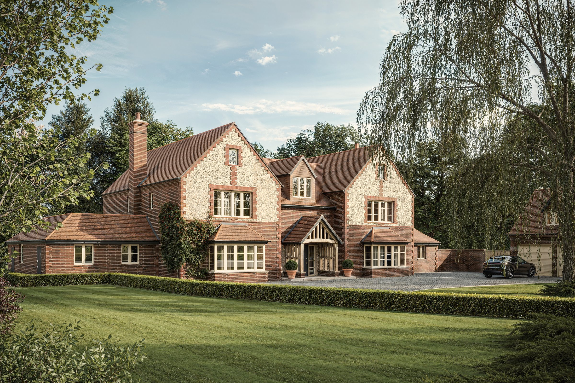 A new brick and flint house near Cromer under clay plain-tile roofs, set behind a lawn among mature trees