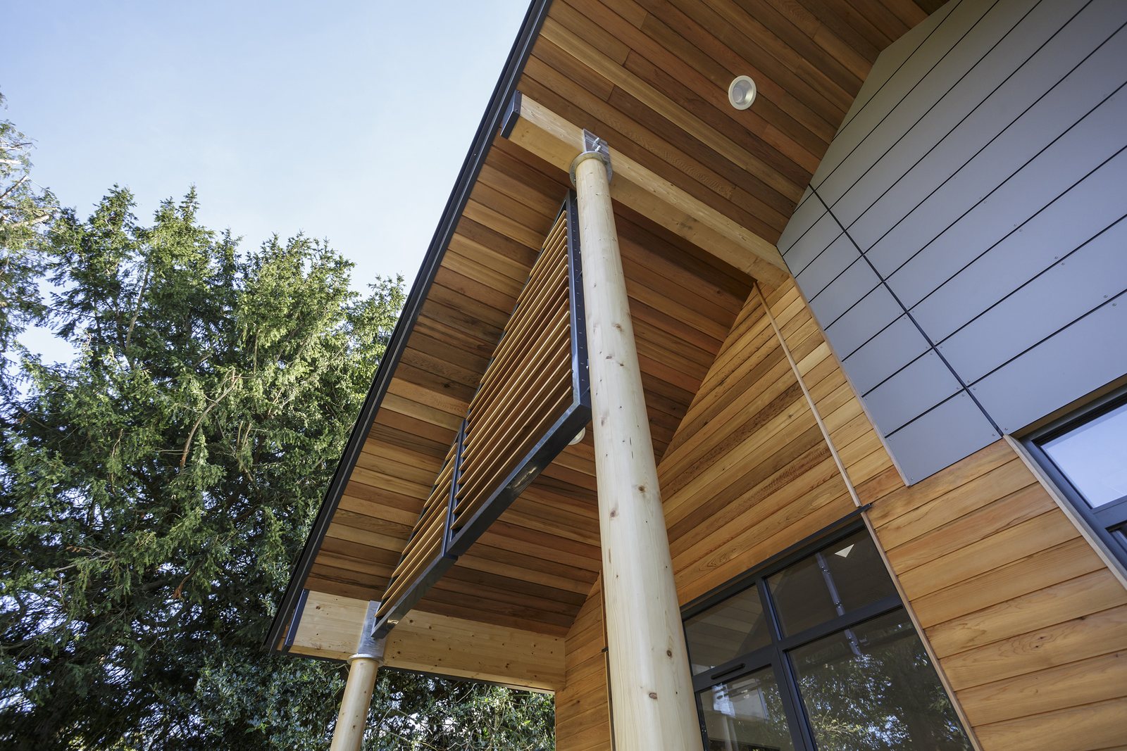 Deep cedar eaves and a round timber column against the trees