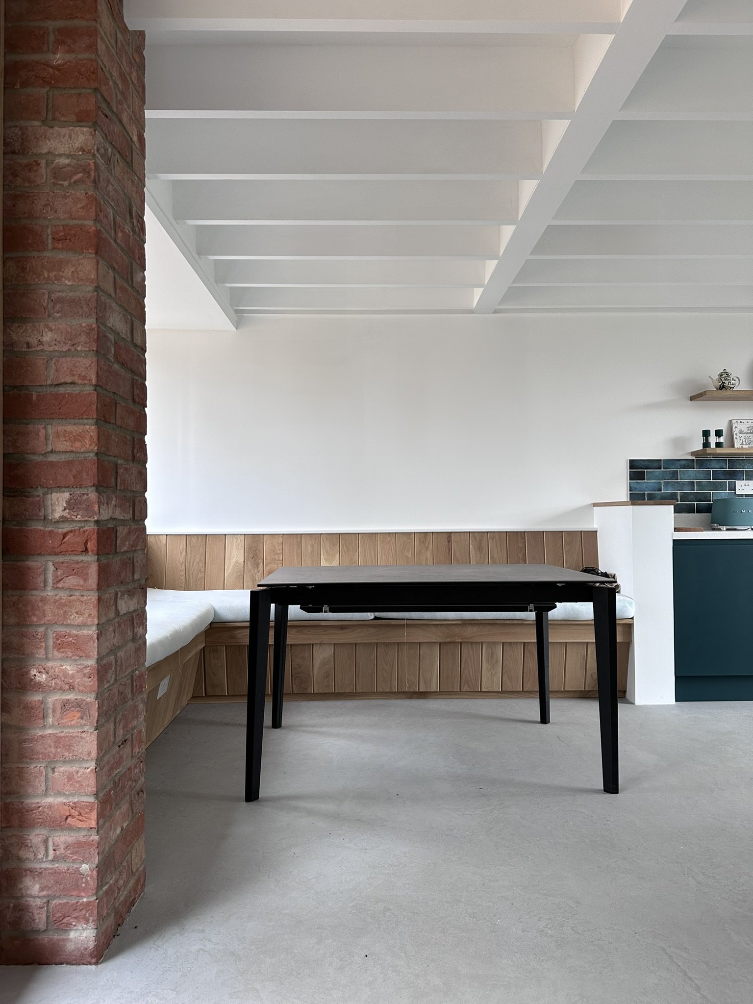 The finished annexe: exposed brick, a painted beamed ceiling, oak bench seating and a small kitchen